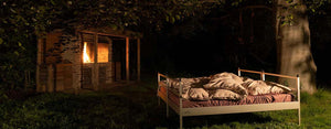 Das Outdoor-Bett SkyHeia steht vor einem Grillplatz mit Lagerfeuer unter einer großen Buche. Es eignet sich für außergewöhnliche Übernachtungen und macht die Nacht zum Erlebnis. Jetzt gibt es dieses Outdoor Bett zum Kauf.